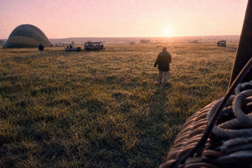 Pale dry grass at sunrise with dew still on the blades, a wicker basket edge and coiled rope at the frame edge, long shadows stretching toward the camera