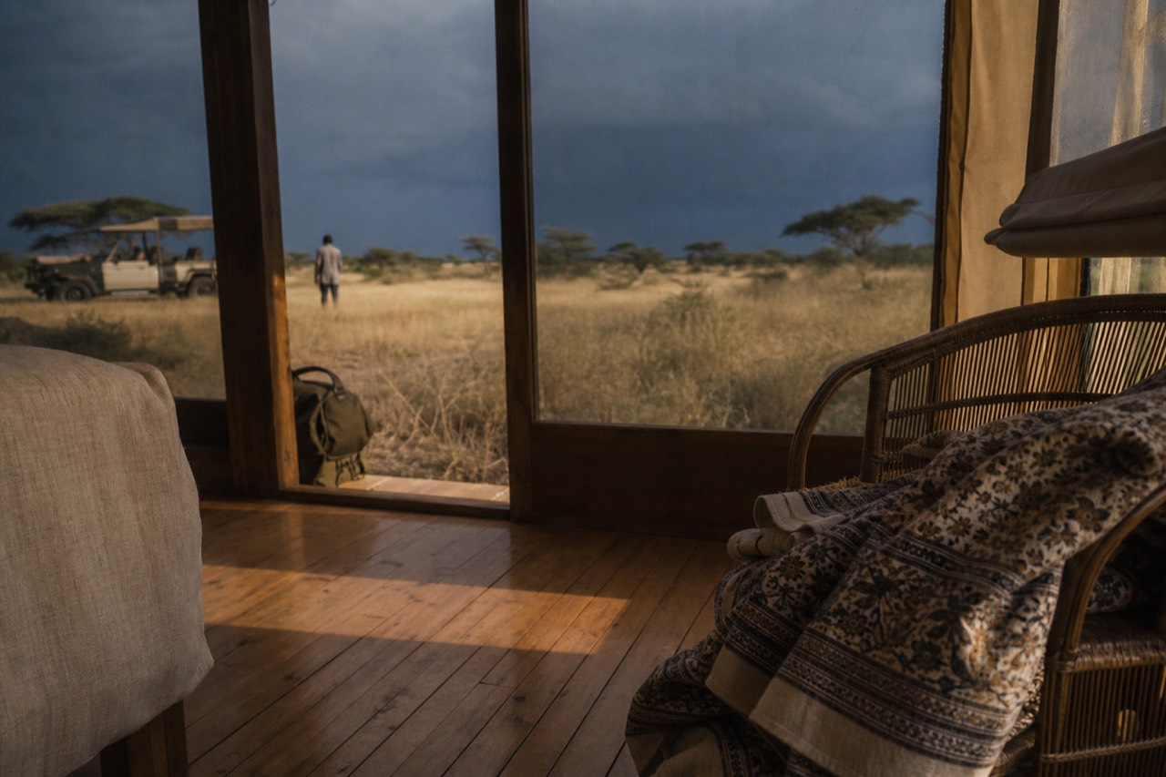 Lightweight linen trousers, a khaki shirt and a printed cotton wrap folded on a rattan chair beside a lodge window with warm afternoon light on the floorboards