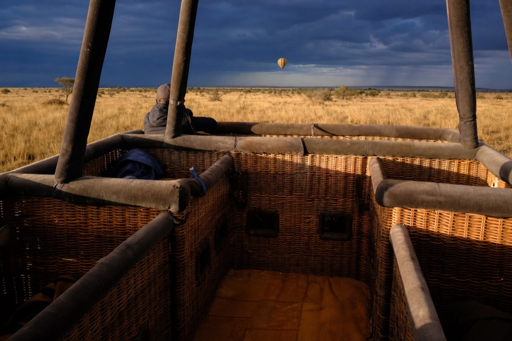 Interior of a wicker balloon basket at dawn showing padded rails and woven passenger compartments, warm low light across the floor