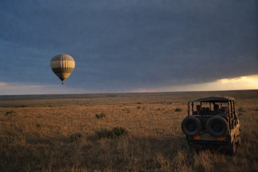 A balloon drifting low over featureless open grassland with the sun just clear of the horizon, no road, building or landmark in any direction