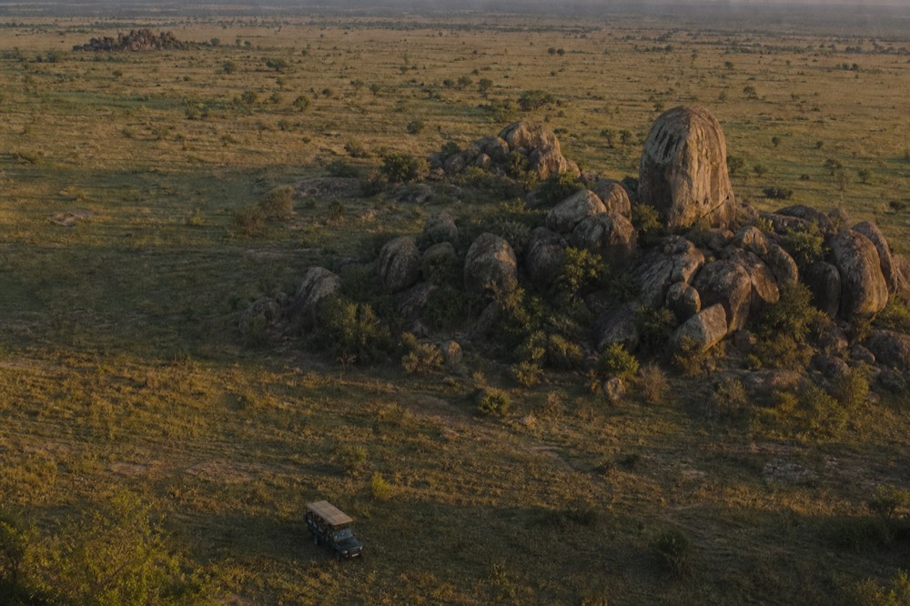 Granite kopjes scattered across flat plains photographed from altitude at sunrise, boulder clusters casting long hard shadows over dry grass