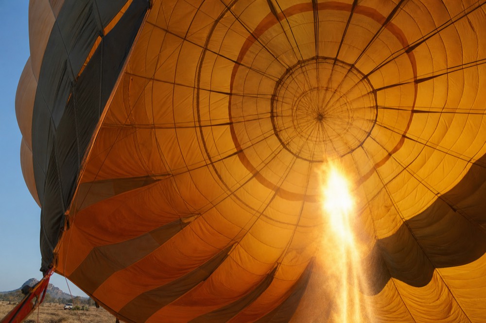 View up into the throat of an inflating balloon envelope from below, fabric panels glowing warm amber as burner light passes through them